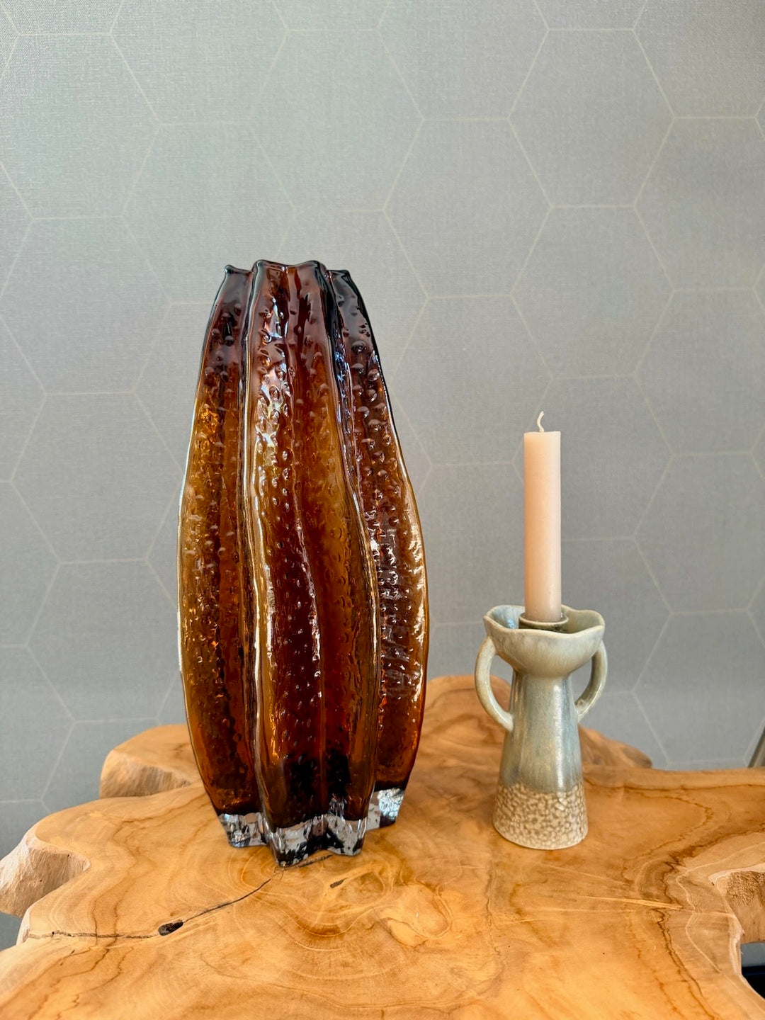 Groene kandelaar van steengoed naast een amberkleurige glazen vaas