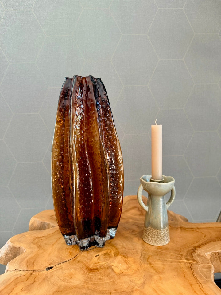 Groene kandelaar van steengoed naast een amberkleurige glazen vaas